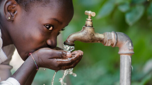 Une petite fille boit de l'eau au robinet.